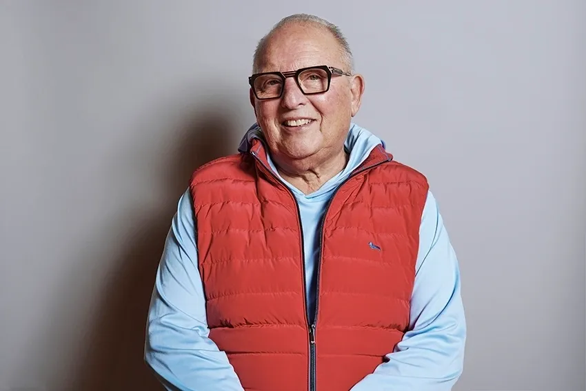 A man in glasses and red vest smiling.